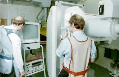 two radiographers wearing lead lined coats, performing fluroscopic procedure and viewing patient on screen