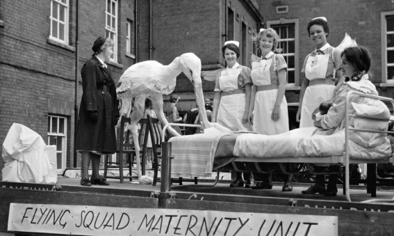 Model stork with mother in bed and maternity staff on back of carnival float