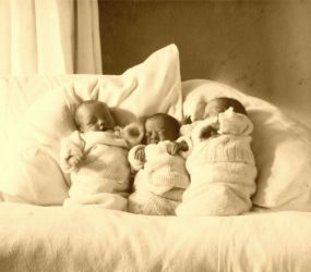 Three babies wrapped up in blankets and propped up pillows