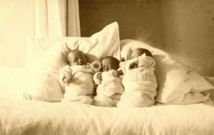 Three babies wrapped up in blankets and propped up pillows