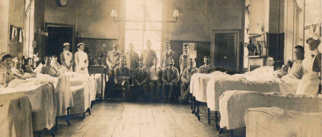 Patients in beds either side of ward and seated at the end with nurses