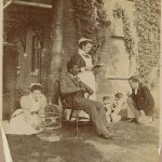 Nurse Mrs Shellcross stands centre, nurse sat on grass beside with a bird cage, man seated, another man on grass with two dogs sat on their hind legs
