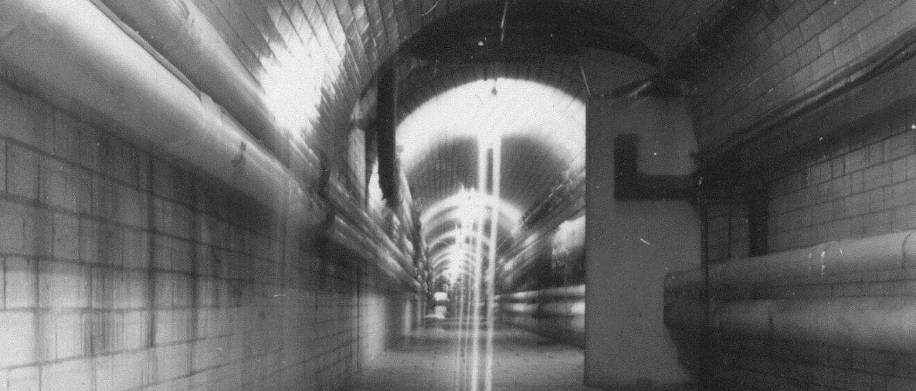 Black and white photo of tunnel with tiles and pipes