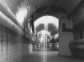 Black and white photo of tunnel with tiles and pipes