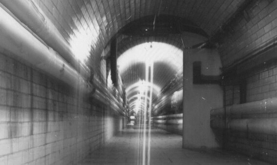 Black and white photo of tunnel with tiles and pipes