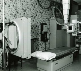 x-ray table and x-ray tube and associated equipment, floral wallpaper on wall behind
