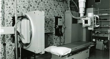 x-ray table and x-ray tube and associated equipment, floral wallpaper on wall behind