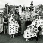 Children in playing card costumes, staff as Mad Hatter, white rabbit etc.. stand next to float