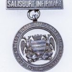 silver metal badge with Salisbury city crest and Infirmary motto