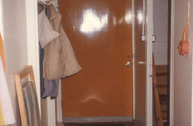 a colour photo of hallway with yellow door, coats and folded deck chair