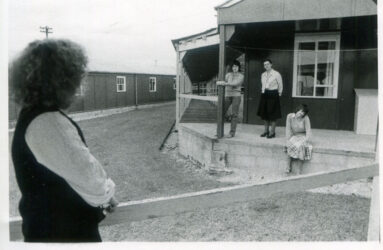 black and white photograph of 3 people outside wooden hut