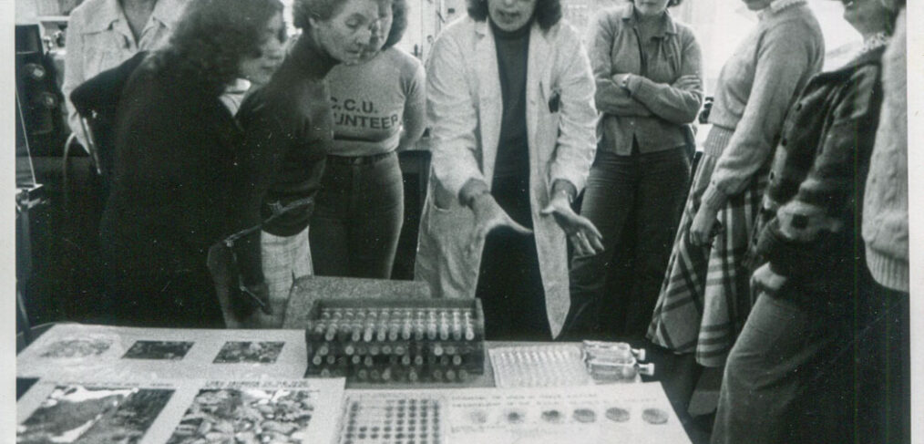 black and white photograph of group of people looking at science experiment