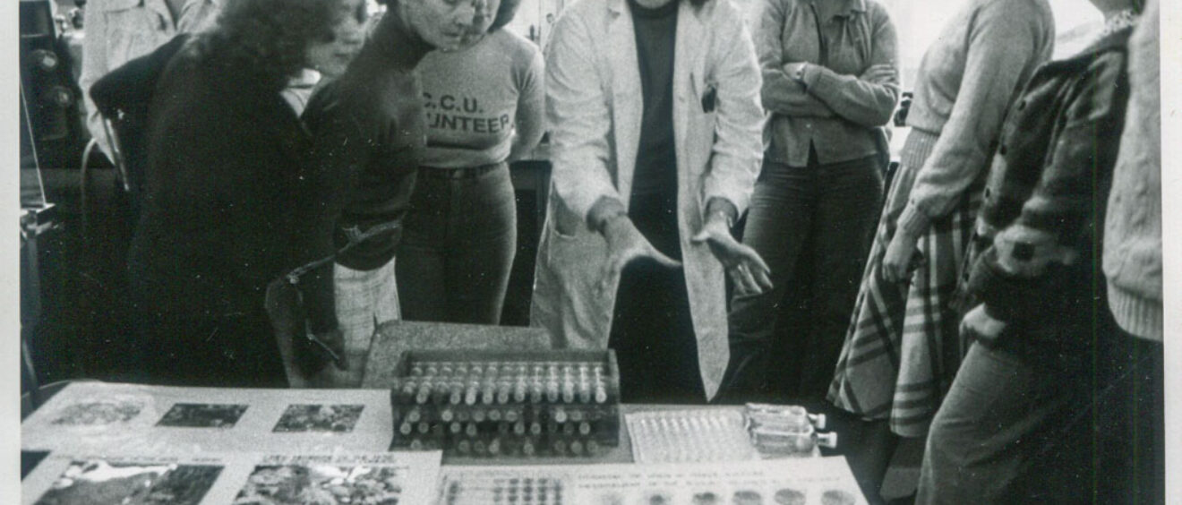 black and white photograph of group of people looking at science experiment