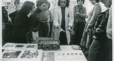 black and white photograph of group of people looking at science experiment