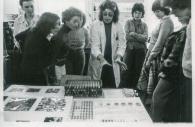 black and white photograph of group of people looking at science experiment
