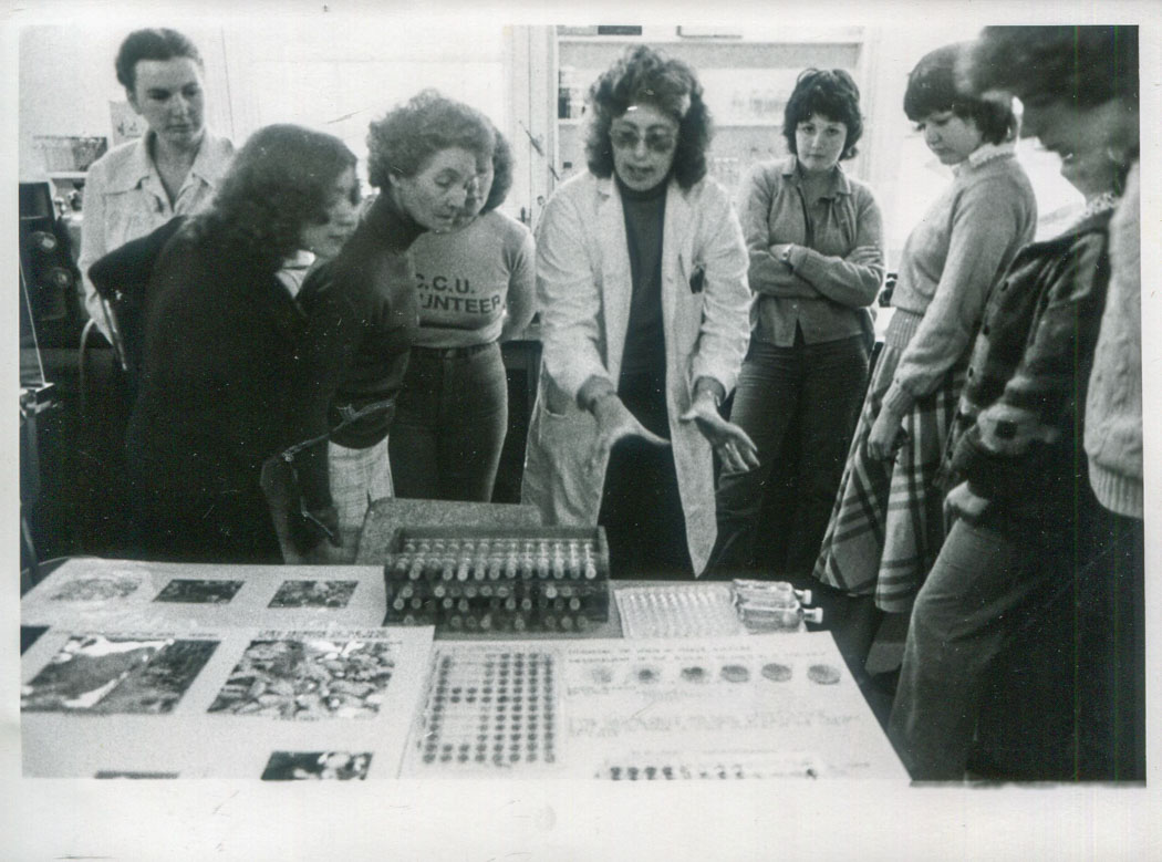 black and white photograph of group of people looking at science experiment