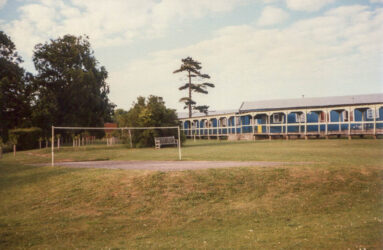 a colour photo of grass sports area next to blue huts