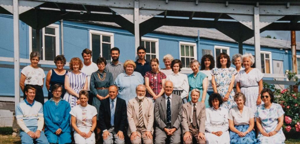 colour photograph of a group of staff in 2 rows in front of blue building