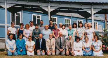 colour photograph of a group of staff in 2 rows in front of blue building