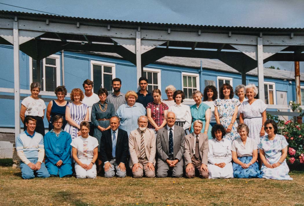 colour photograph of a group of staff in 2 rows in front of blue building