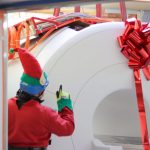 crane operator dressed as elf guiding MRI scanner with red bow on through wall
