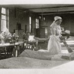 Nurse handing drink or medication to soldier on ward, flowers on central table