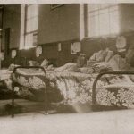 Soldiers sitting up in bed, floral and leaf patterned covers on the bed