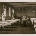 Nurse doing her rounds, metal beds line both sides of the ward