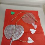 sheer fabric leaf shapes, cut out hearts from green and white paper, string arranged on red tissue paper inside lamination pouch