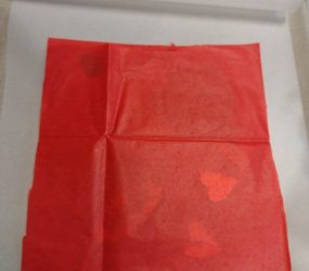 2nd piece of red tissue paper laid over cut out items inside lamination pouch