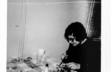 black and white photograph showing person sat a table eating meal