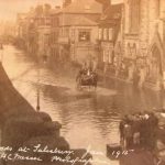 View of flooded street in front of the Infirmary building, horse and cart moving through the flood water