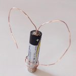 copper wire coiled into heart shape around AA battery balanced on two magnets