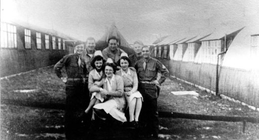 Soldiers and nurses posing for photo between Nissen huts