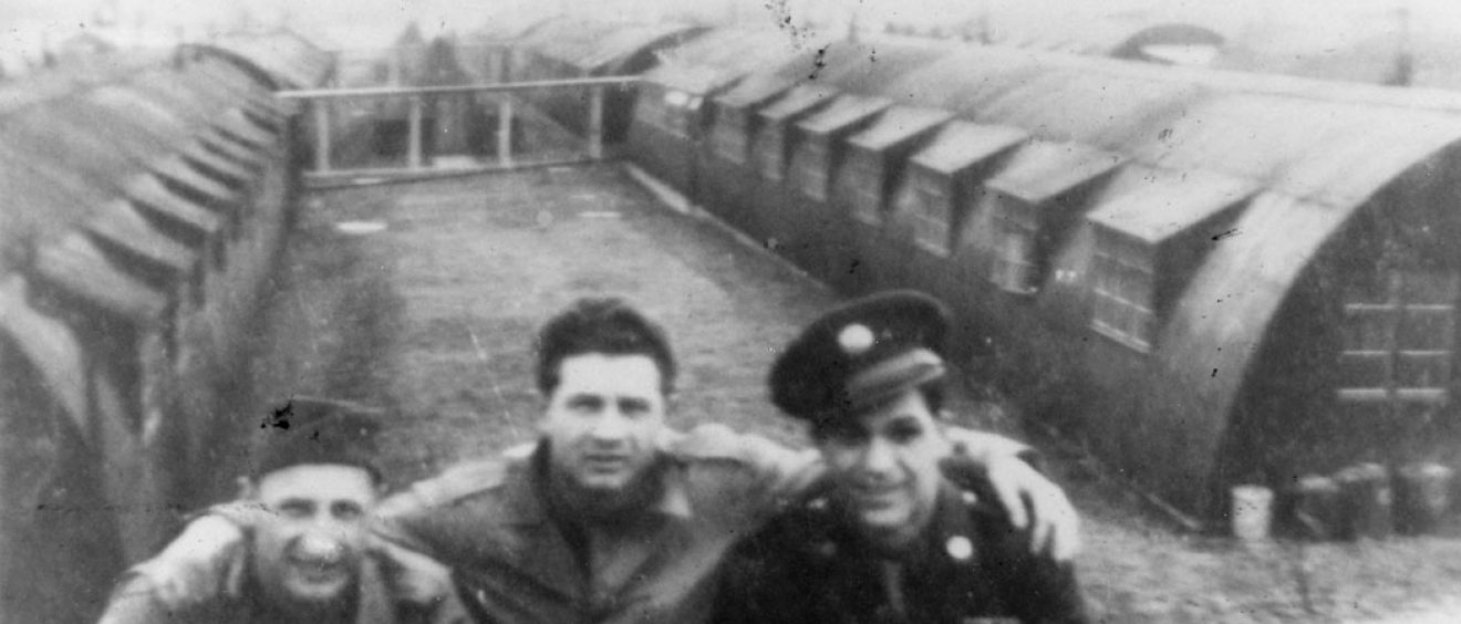 3 soldiers posing for photo between Nissen huts