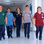 nurses in scrubs of various colors walking along corridor