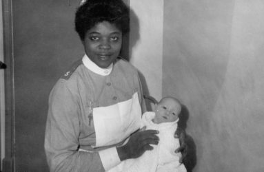 Black nurse holding baby wrapped in shawl