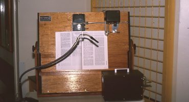 large wooden board holding a text book with tube attachment and device to turn the page
