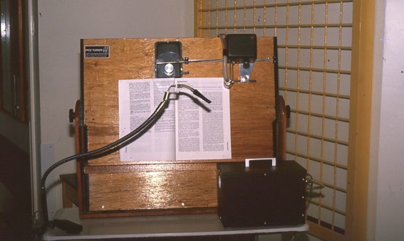 large wooden board holding a text book with tube attachment and device to turn the page