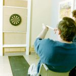 man in wheelchair blowing a pipe with dart aimed at dart board