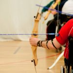 man in wheelchair drawing back bow preparing to shoot an arrow