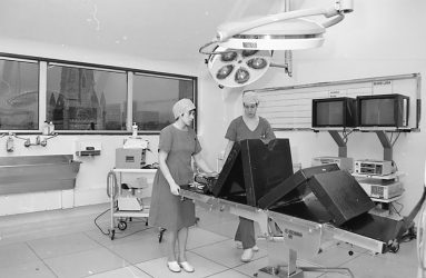 staff in scrubs adjust the operating table, view to city centre visible through window